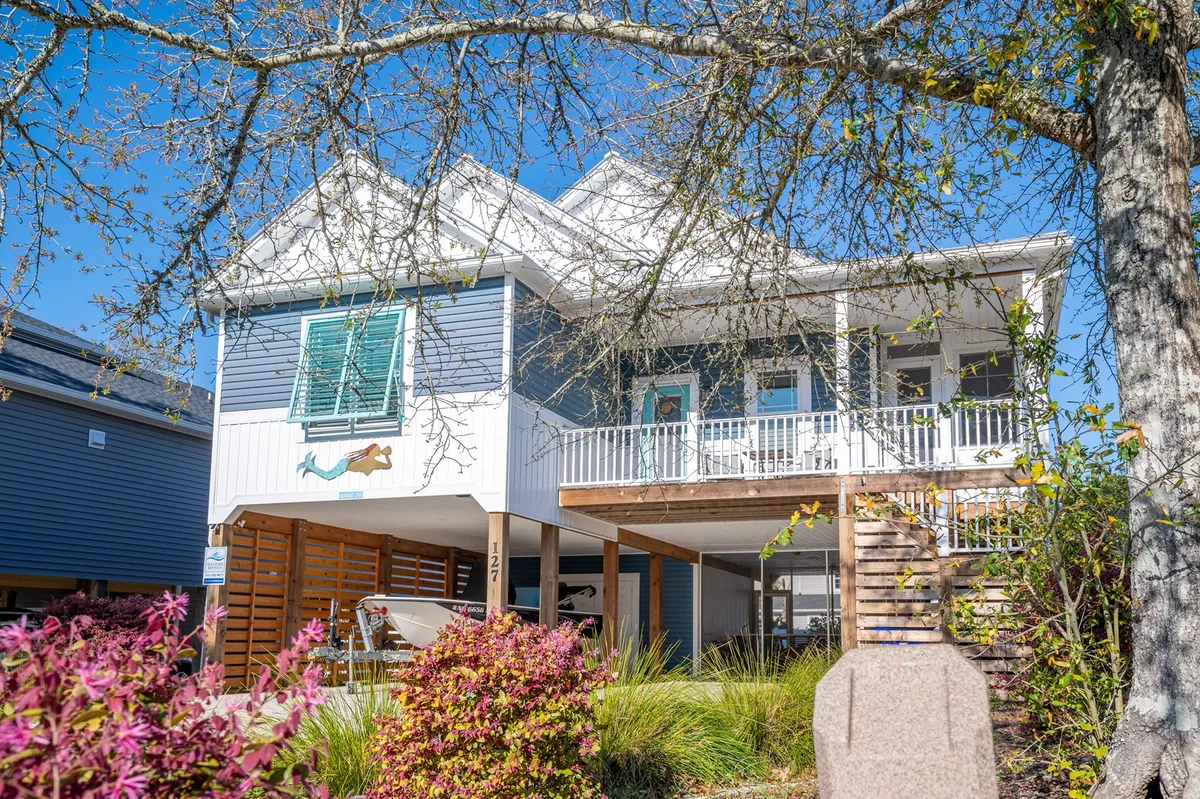 A cheerful exterior shot showing the house's welcoming facade, front porch with seating, and vibrant, colorful plants. The porch provides a comfortable spot to unwind after a day of activities, and the landscaping hints at the home's connection to nature.
