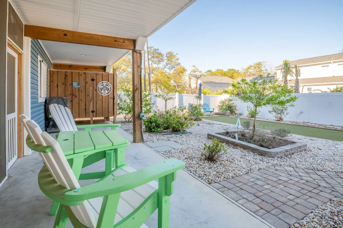 A welcoming yard features green Adirondack chairs, colorful flower beds, a paved walkway, and a decorative fence. The space feels tranquil and is ideal for relaxing, playing lawn games, or enjoying social gatherings.