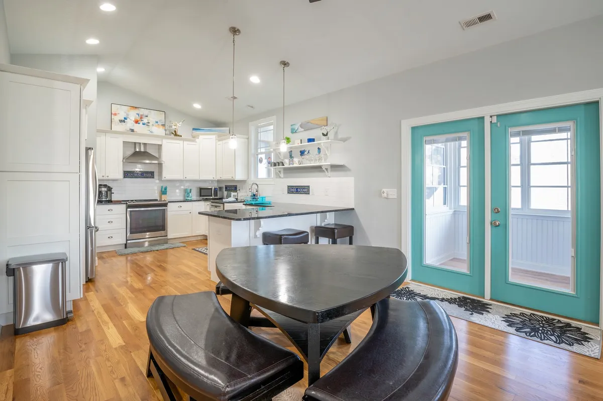 A warm, welcoming interior shot showcasing a black dining table, turquoise doors, a kitchen island, and white cabinetry. The setup suggests an open-concept space ideal for family meals and group gatherings, with ample dining and prep space for cooking together.