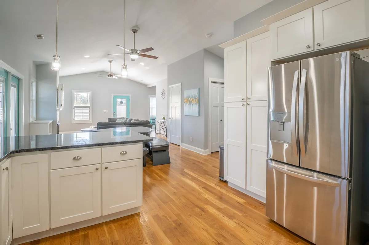 A modern kitchen with a central island, stainless steel refrigerator, open layout, and ample natural light streaming in through the windows. The space is designed for both cooking and gathering, with plenty of room for multiple people.