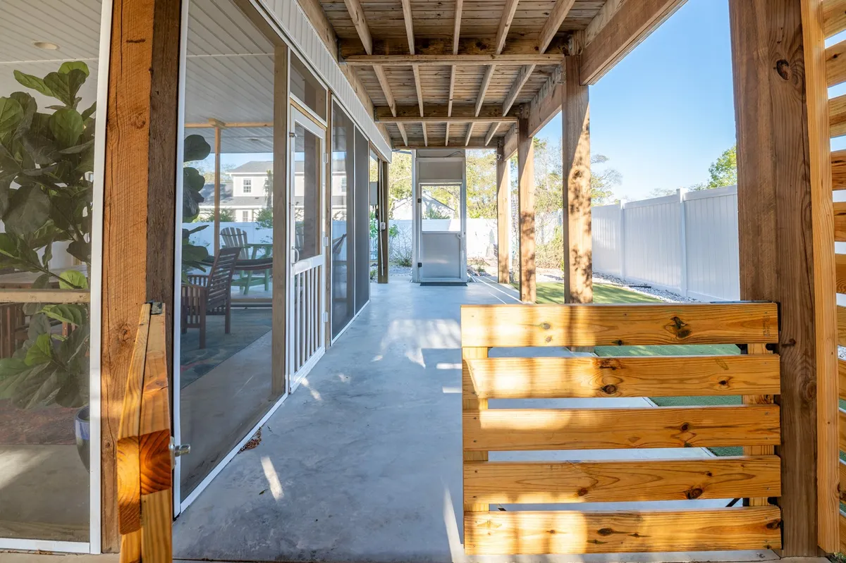 A tranquil, screened porch with sturdy wooden beams, outdoor lounge furniture, and screened walls. This inviting setting is perfect for relaxing, entertaining, or enjoying a meal shielded from insects, with views of the outdoors framed by the mesh walls. The porch exudes comfort and connection to nature, hinting at both privacy and breezy openness.
