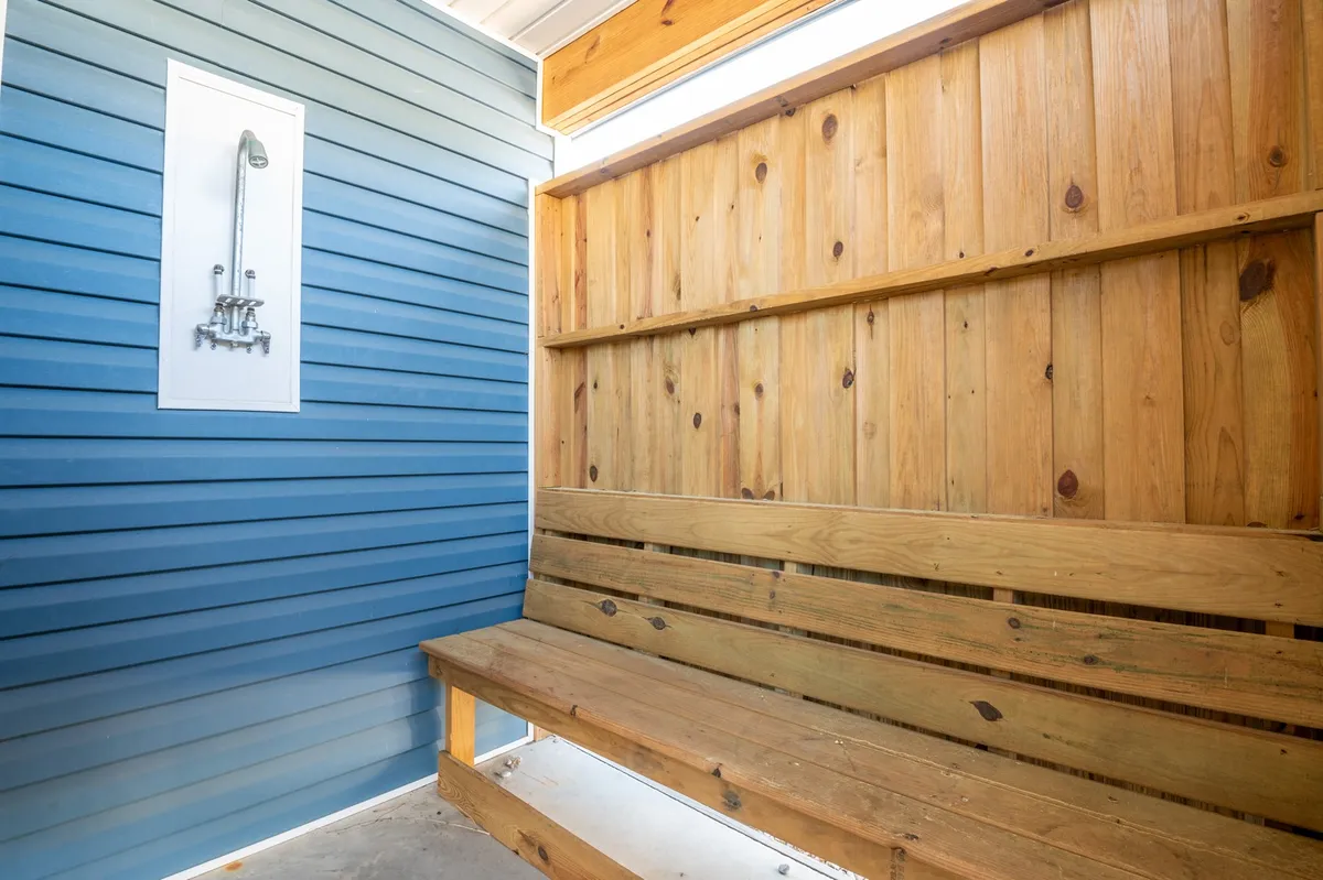 A cozy and practical outdoor shower area with a wooden bench and blue-accented wooden walls. The space is thoughtfully designed for rinsing off after beach days, providing privacy and a touch of coastal charm. It's functional, comfortable, and reflects the relaxation ethos of the property.