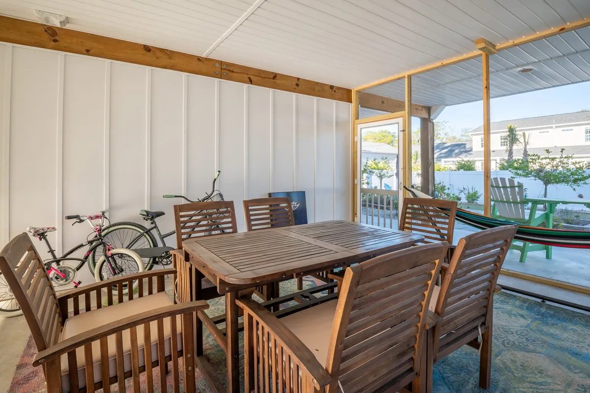 A wooden dining table is surrounded by comfortable chairs, with large glass doors providing a glimpse of a hammock outside and bicycles in the corner, suggesting an active, family-friendly environment.