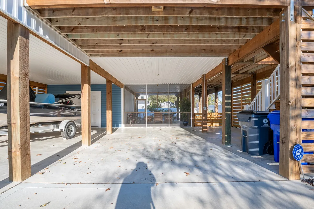 This exterior image captures the wooden support beams of the house, a boat on a trailer ready for aquatic adventures, an outdoor seating area, and a staircase leading up to the main living space. The scene evokes a relaxed, coastal vibe and hints at the property's proximity to water-based activities.