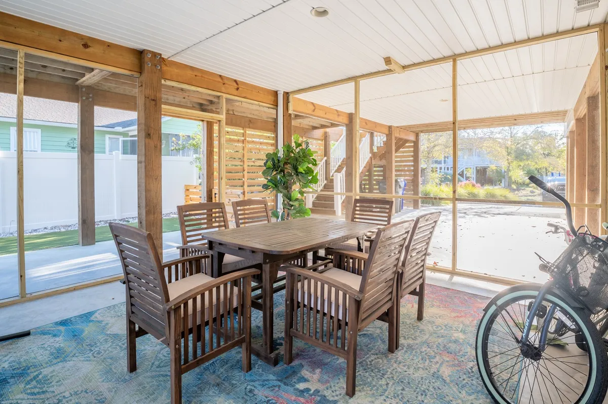 An interior scene featuring a wooden dining table with eight matching chairs, a potted plant as a centerpiece, and a bicycle visible in the background. The space is bright, cozy, and ideal for group gatherings, meals, or planning the next day's adventures.